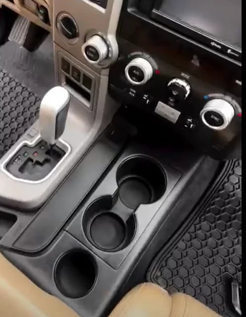 Car interior showing center console with cup holders and automatic transmission shifter in beige and black trim