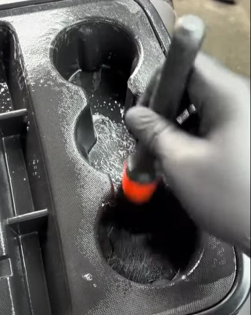 Hand holding soldering iron inserting into a black speaker with orange heated tip