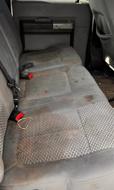 Dirty vehicle interior with worn fabric seats and visible dust accumulation on rear bench seating