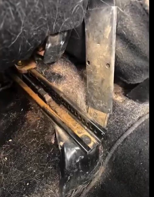Close-up of a metal vehicle door hinge showing rust, weathered components, and mechanical wear